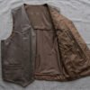 An open leather vest laid flat showing an interior holster-style pocket positioned at mid-chest on the left panel, reinforced stitching visible around the pocket edge. Studio lighting, neutral dark background, no firearm shown — focus entirely on the pocket construction.